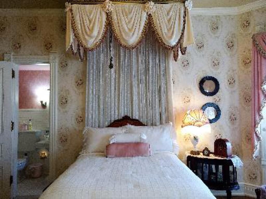 Une chambre à coucher avec un lit à baldaquin, une table de chevet avec une lampe et un miroir au mur.