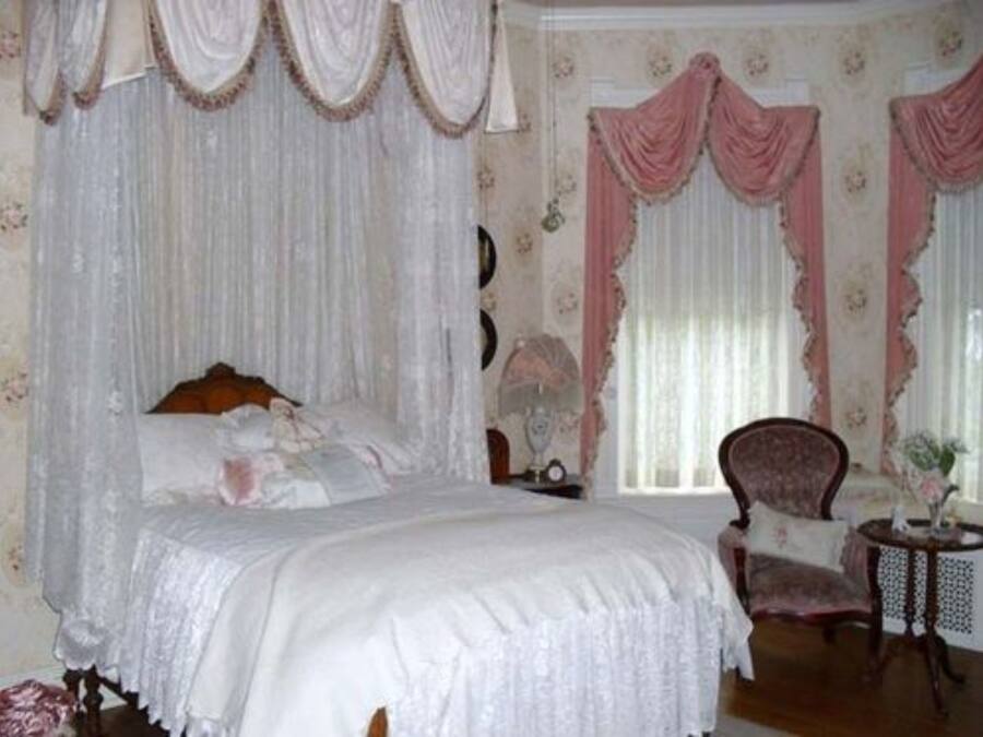 Un dormitorio con cama a dosel, una silla y una mesita.