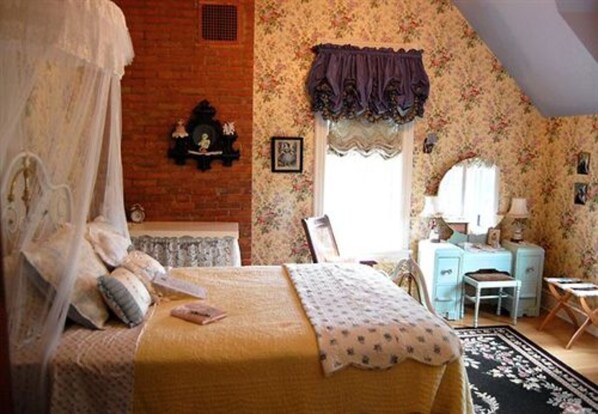 Quarto com cama, uma cadeira, escrivaninha e janela com cortinas.