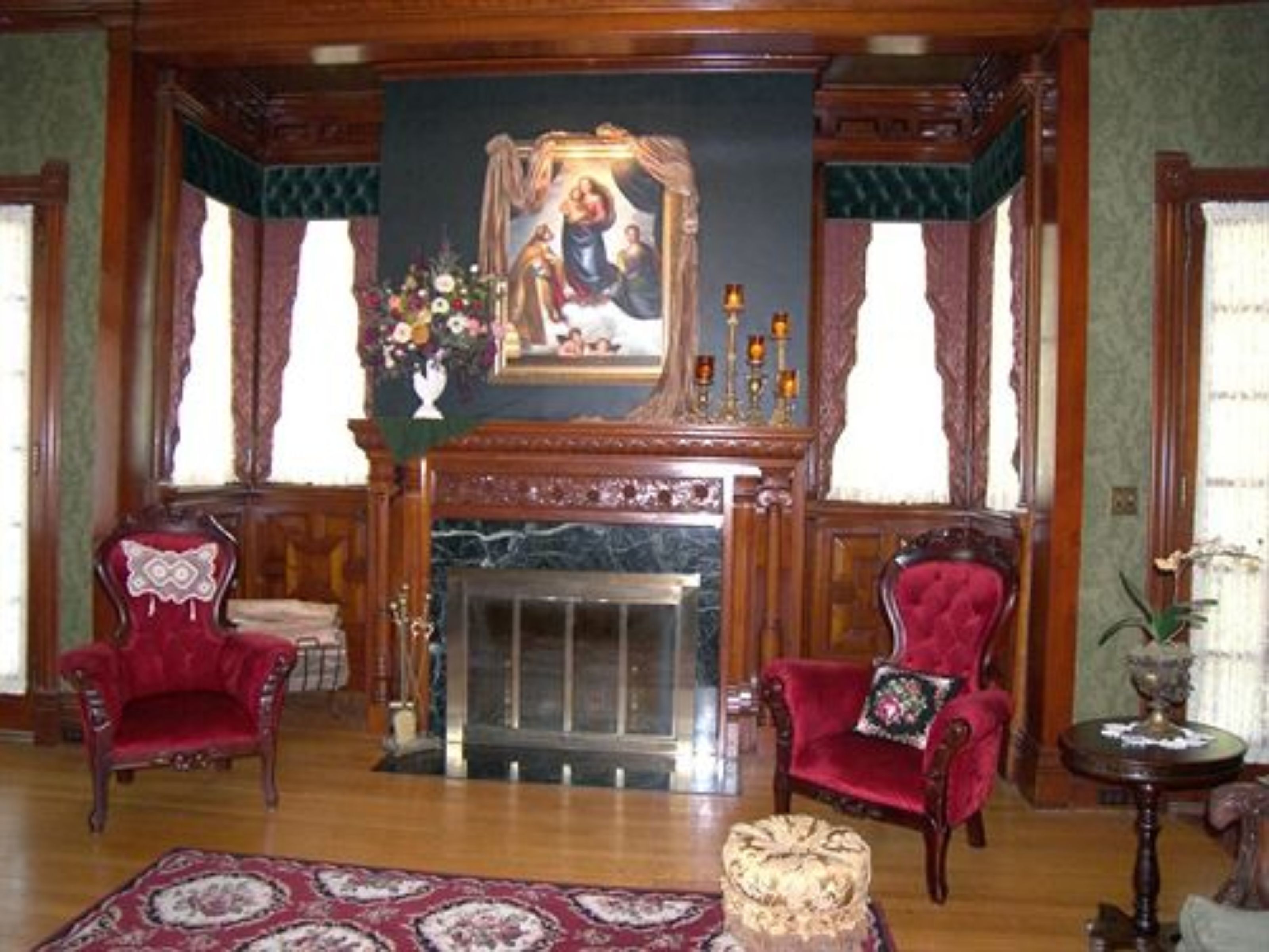 A room with a fireplace, two red armchairs, a patterned rug, and a painting above the mantel.