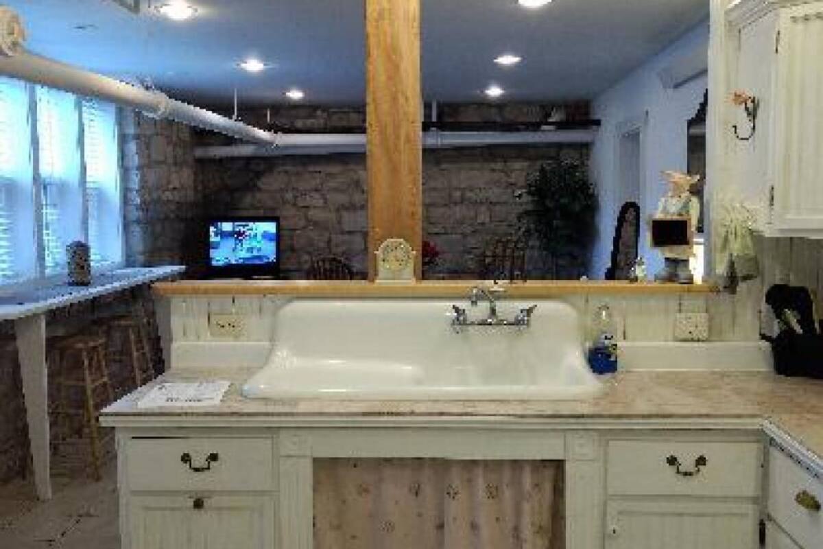 A kitchen with a white sink, wooden cabinets, and a stone wall in the background.
