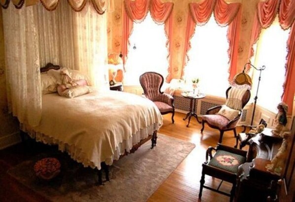A bedroom with a four-poster bed, a sitting area with a chair and a small table, and a lamp. - Alexander Mansion Bed and Breakfast (Winona)