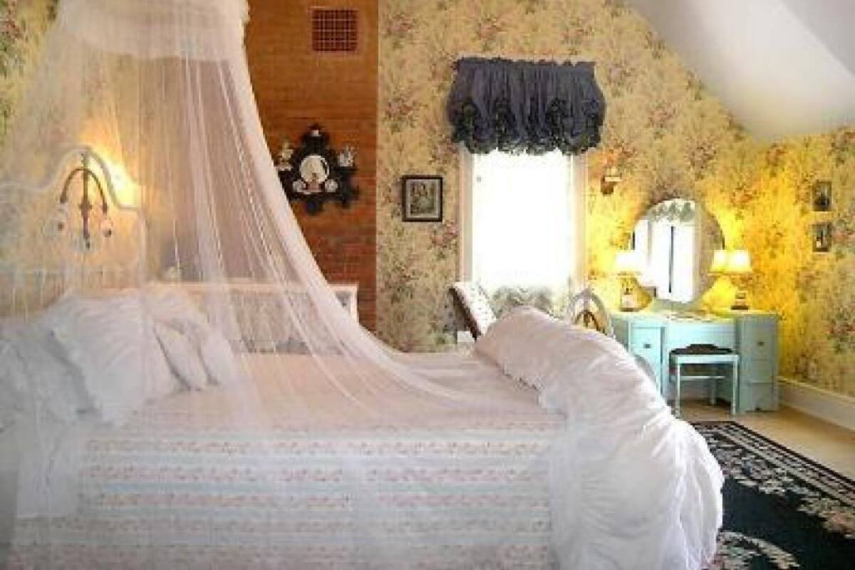 A bedroom with a canopy bed, a desk with a chair, a mirror, and a window with a curtain.