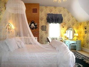 Un dormitorio con cama a dosel, un escritorio con silla, un espejo y una ventana con cortina.
