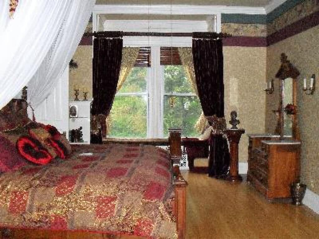 Une chambre à coucher avec un grand lit, une commode, un miroir et une fenêtre avec des rideaux.