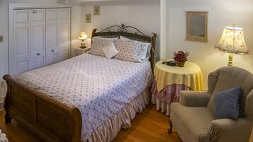 A bedroom with a wooden bed, a bedside table with a lamp, a chair, and a small table with a lamp.
