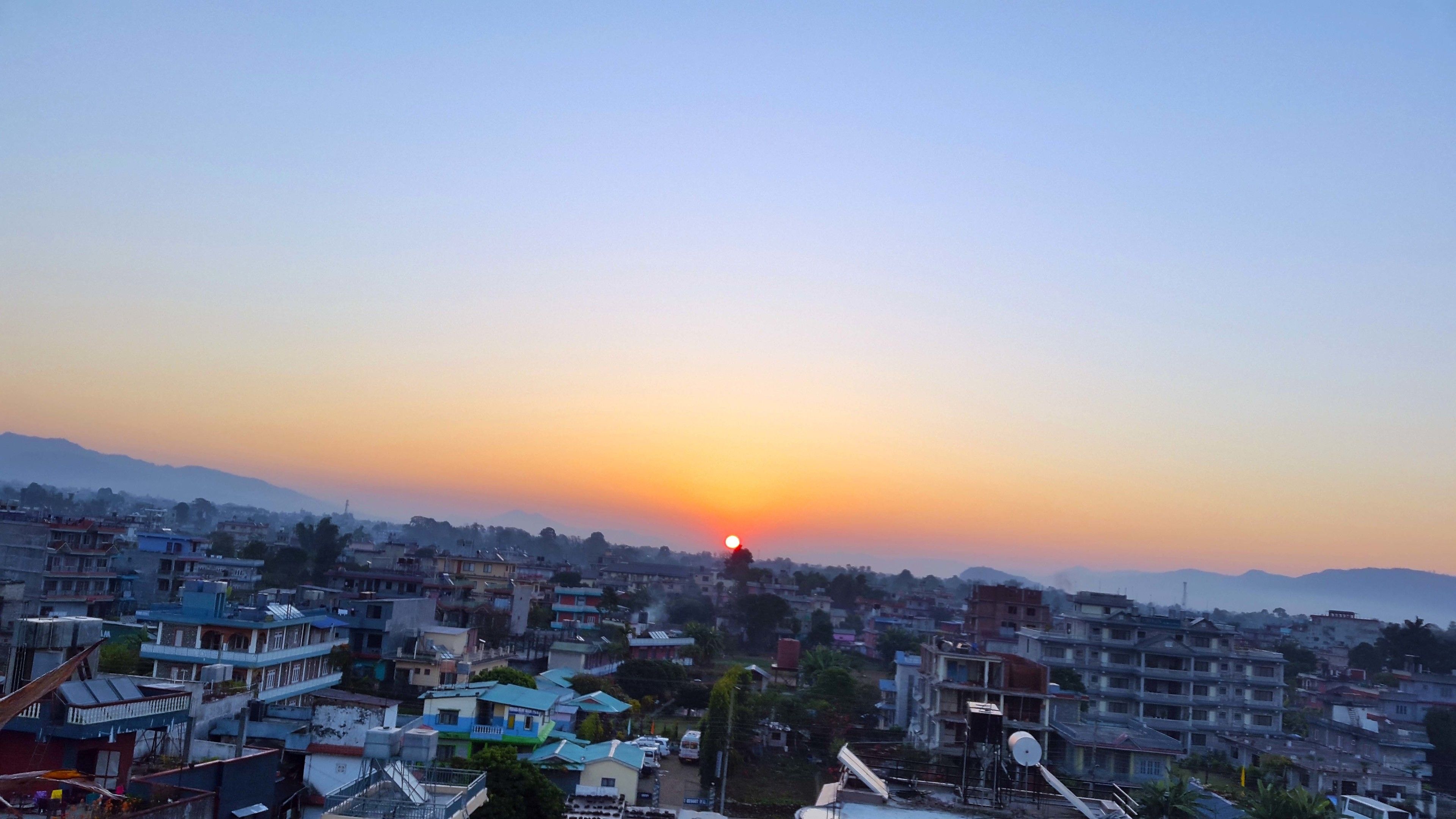Un paisaje urbano con el sol poniéndose al fondo, mostrando edificios apretados y un cielo despejado.