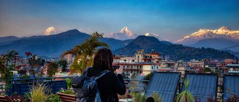 A person taking a photo of a mountain range with a city in the background.