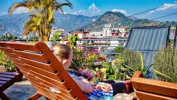A person relaxing on a wooden bench with a view of a mountain and buildings in the background. - Hotel Grand Holiday (Pokhara)