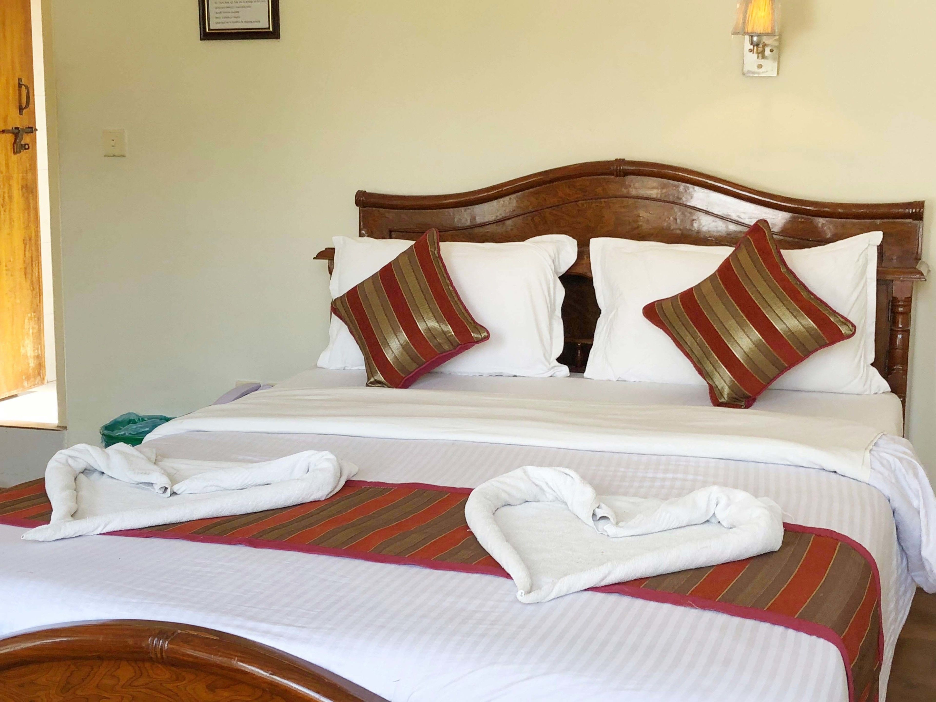 A neatly made bed with white linens and striped pillows, a wooden headboard, and a bedside table with a lamp.