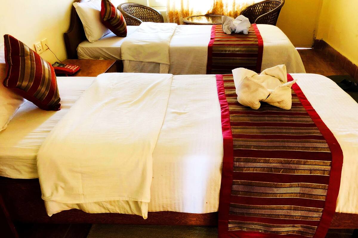 Two single beds with white linens and red-striped bed runners, a small table with a telephone, and wicker chairs.