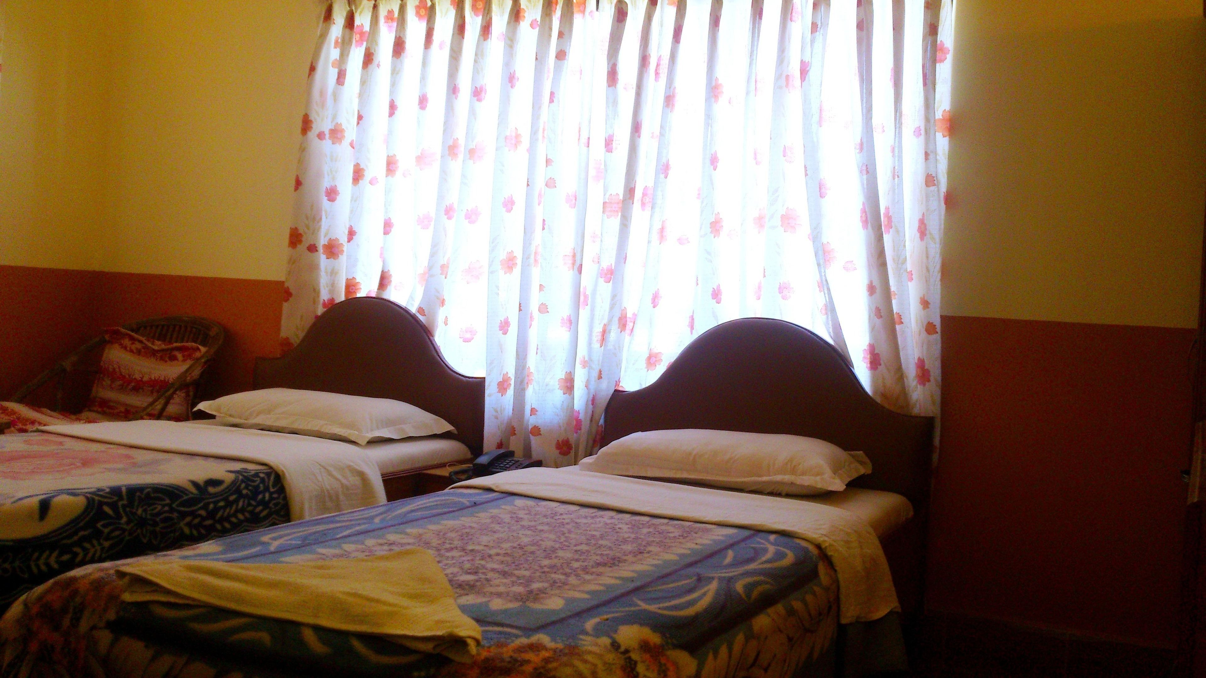 Quarto com duas camas, cada uma com cabeceira e almofadas, e uma cadeira com um assento floral.