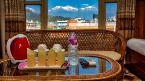 A wicker chair with a glass table, a red kettle, a bottle of water, and a remote control. - Hotel Grand Holiday (Pokhara)