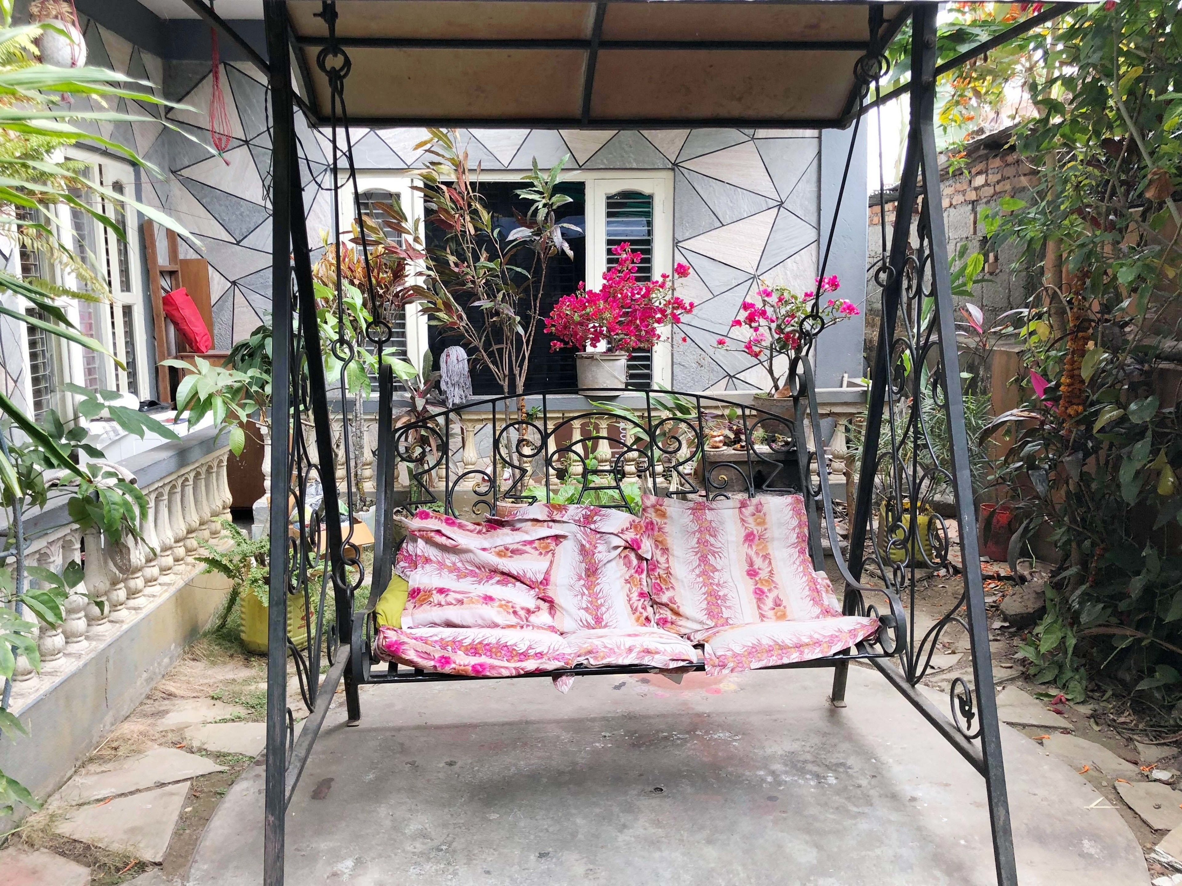 A garden with a swing chair, potted plants, and a building in the background.