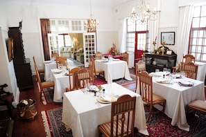 Uma sala de jantar com várias mesas postas para refeição, cadeiras de madeira e um candelabro.
