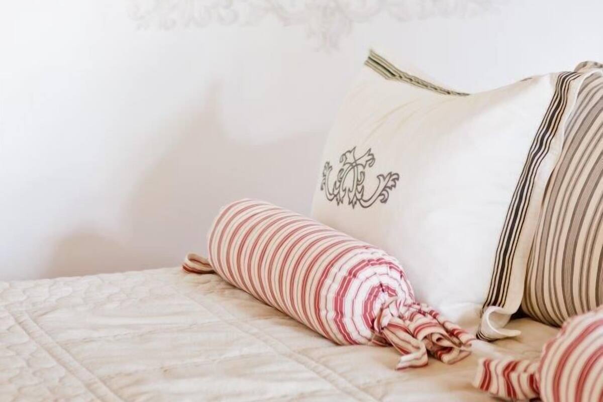Un dormitorio ordenado con cama, almohadas y una obra de arte enmarcada de flores en la pared.