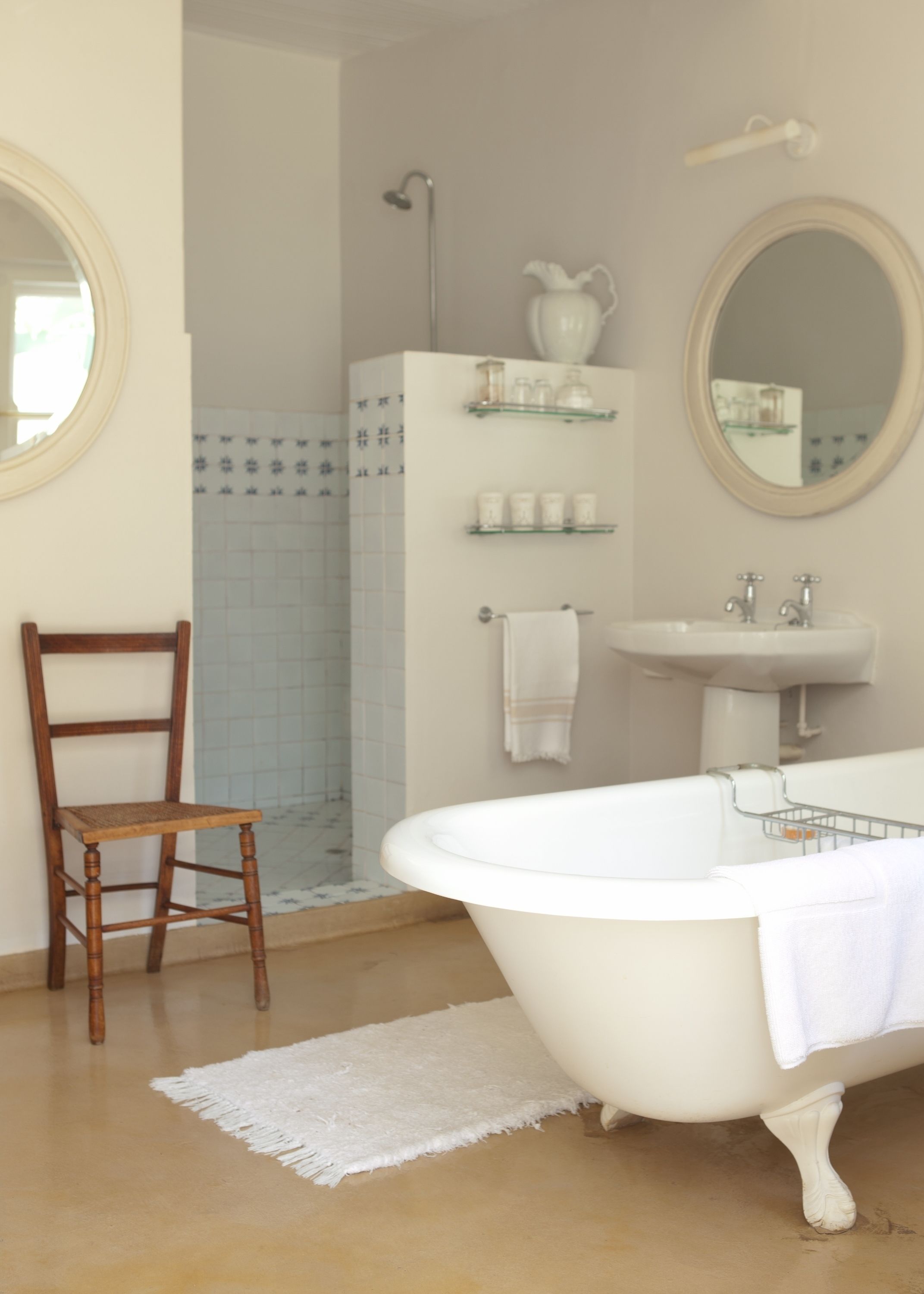 Un baño con una silla de madera, una bañera blanca, un lavamanos y un espejo.