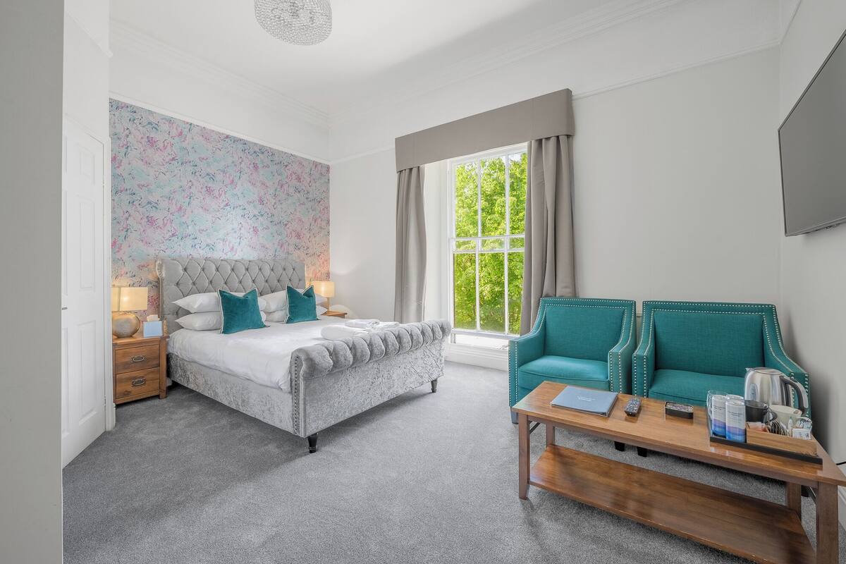 A bedroom with a bed, a sofa, a coffee table, and a window with curtains.