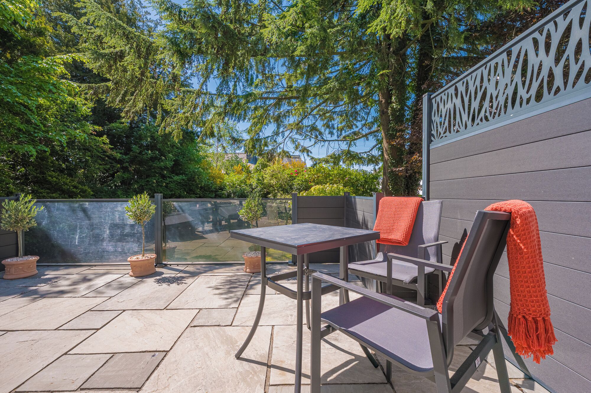 Une terrasse extérieure avec une table et des chaises, des plantes en pot et une clôture décorative.