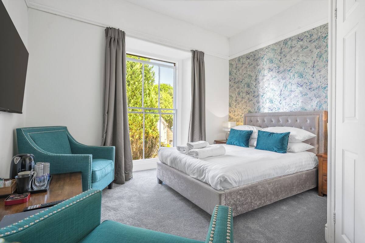 A hotel room with a bed, a chair, a nightstand, and a window with curtains.