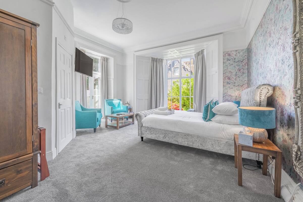 A bedroom with a bed, two chairs, a small table, and a lamp.
