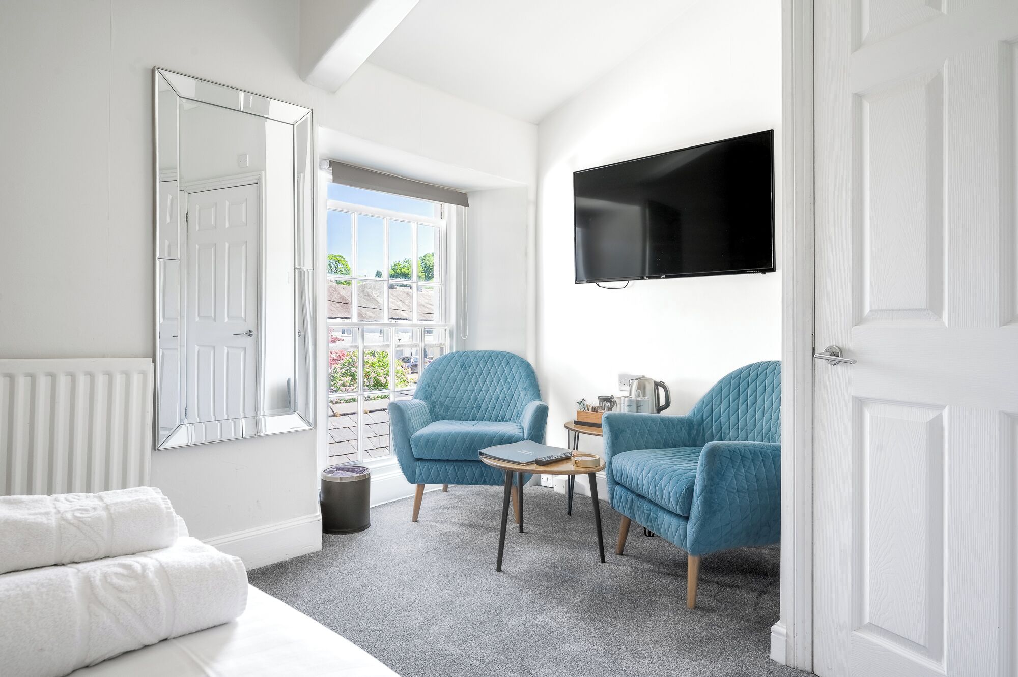 A bright room with a large window, a flat-screen TV, and two blue armchairs.
