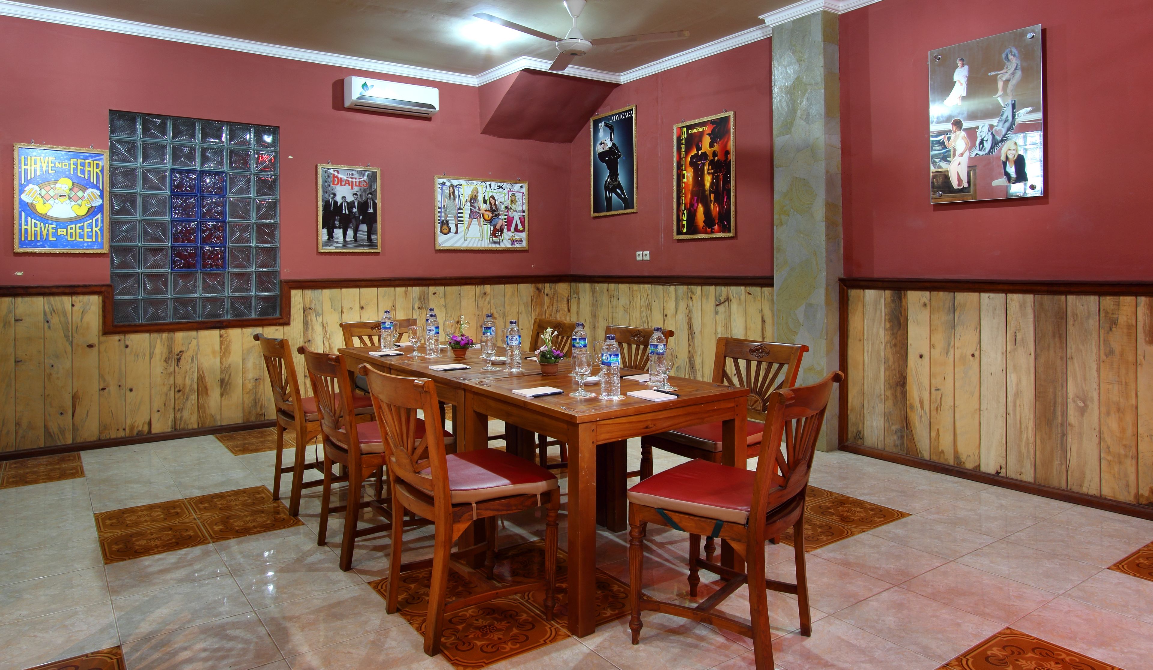 Comedor con una mesa y sillas de madera, rodeado de paredes rojas decoradas con carteles enmarcados.