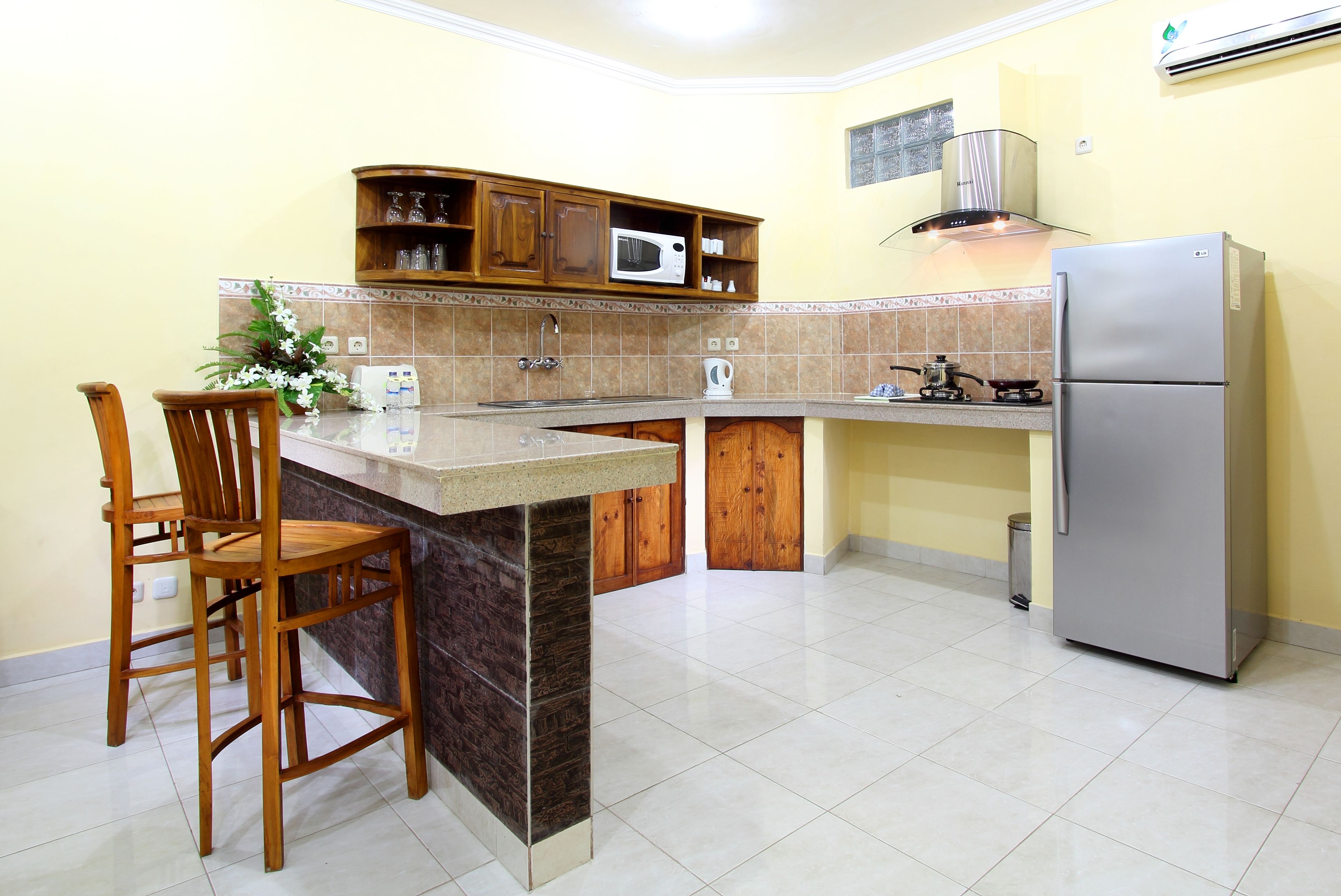 Una cocina con una isla central, sillas de madera, microondas, estufa y refrigerador.