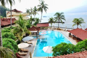 A resort with a swimming pool, lounge chairs, umbrellas, and a view of the sea. - Bali Palms Resort (Manggis)