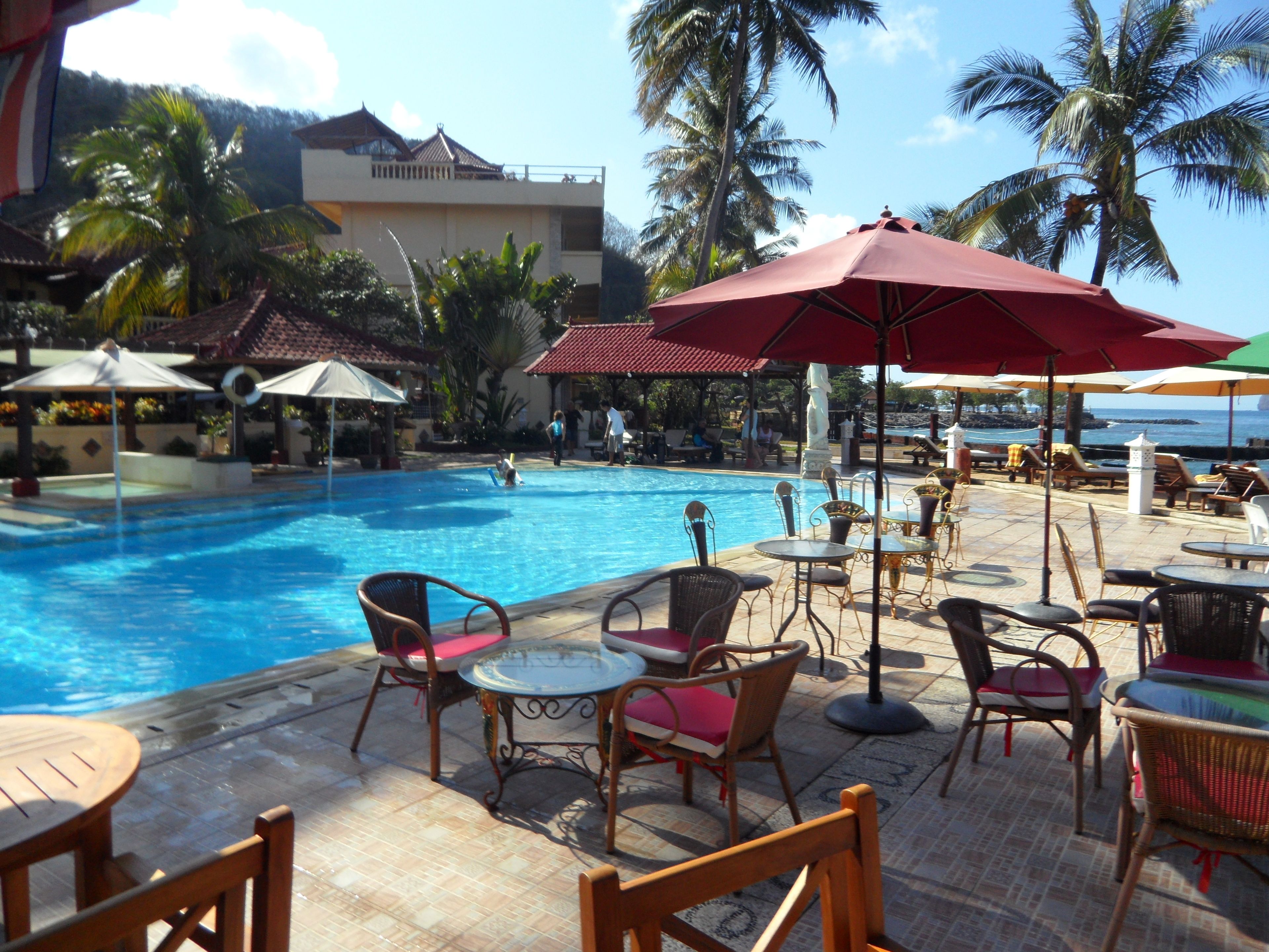 A poolside area with lounge chairs and umbrellas, a clear blue pool, and a building with a tiled roof in the background.