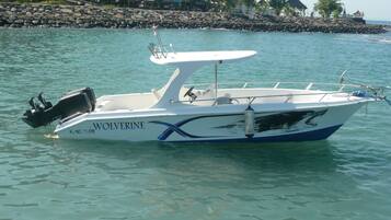 Un velero blanco y azul llamado 'Wolverine', con motor y zona de asiento, amarrado en una orilla tranquila.