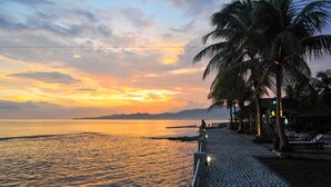 Eine Küstenpromenade mit Palmen und Sonnenuntergang.