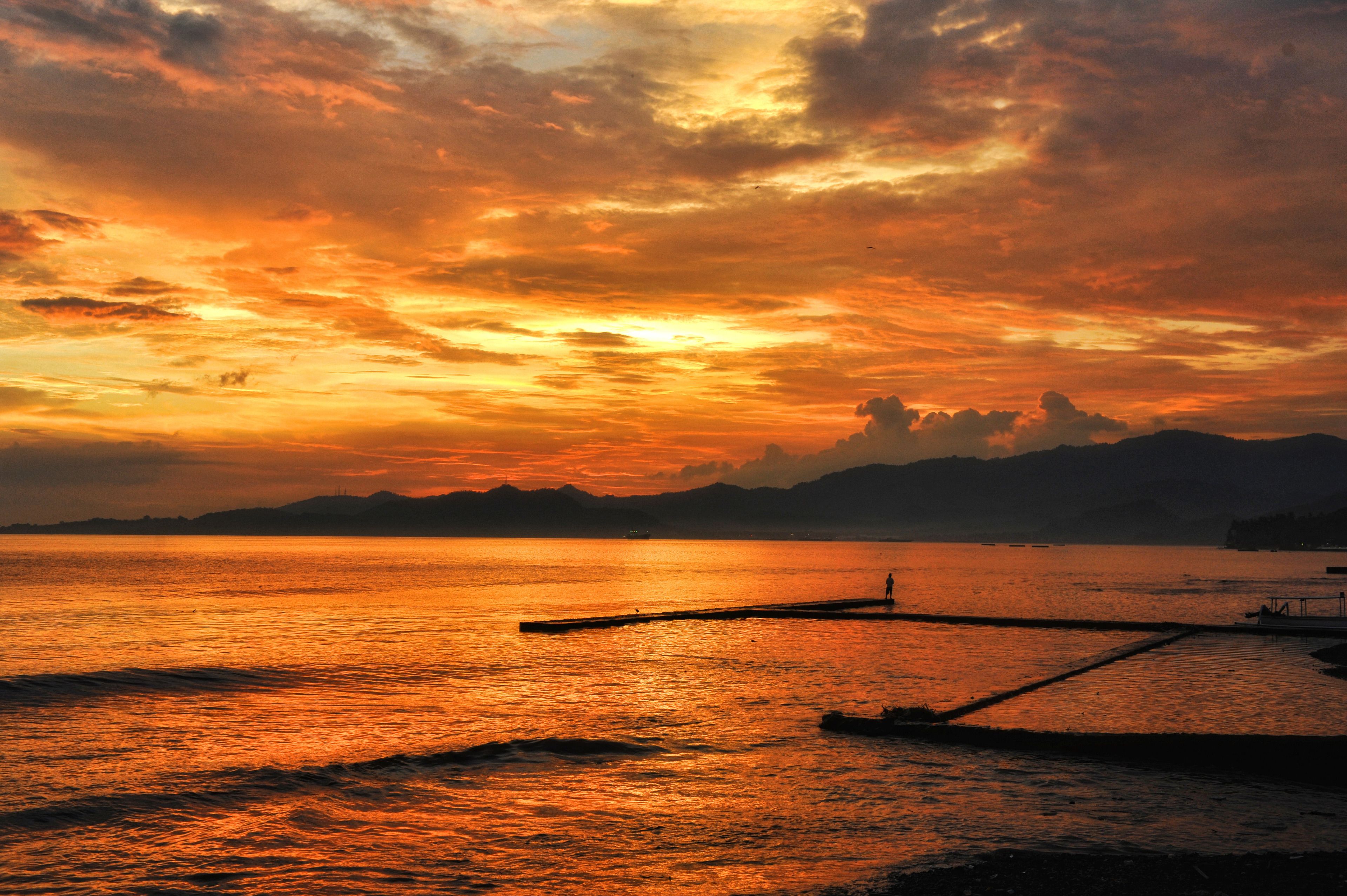 A sunset over a calm body of water with a dock extending into the water.
