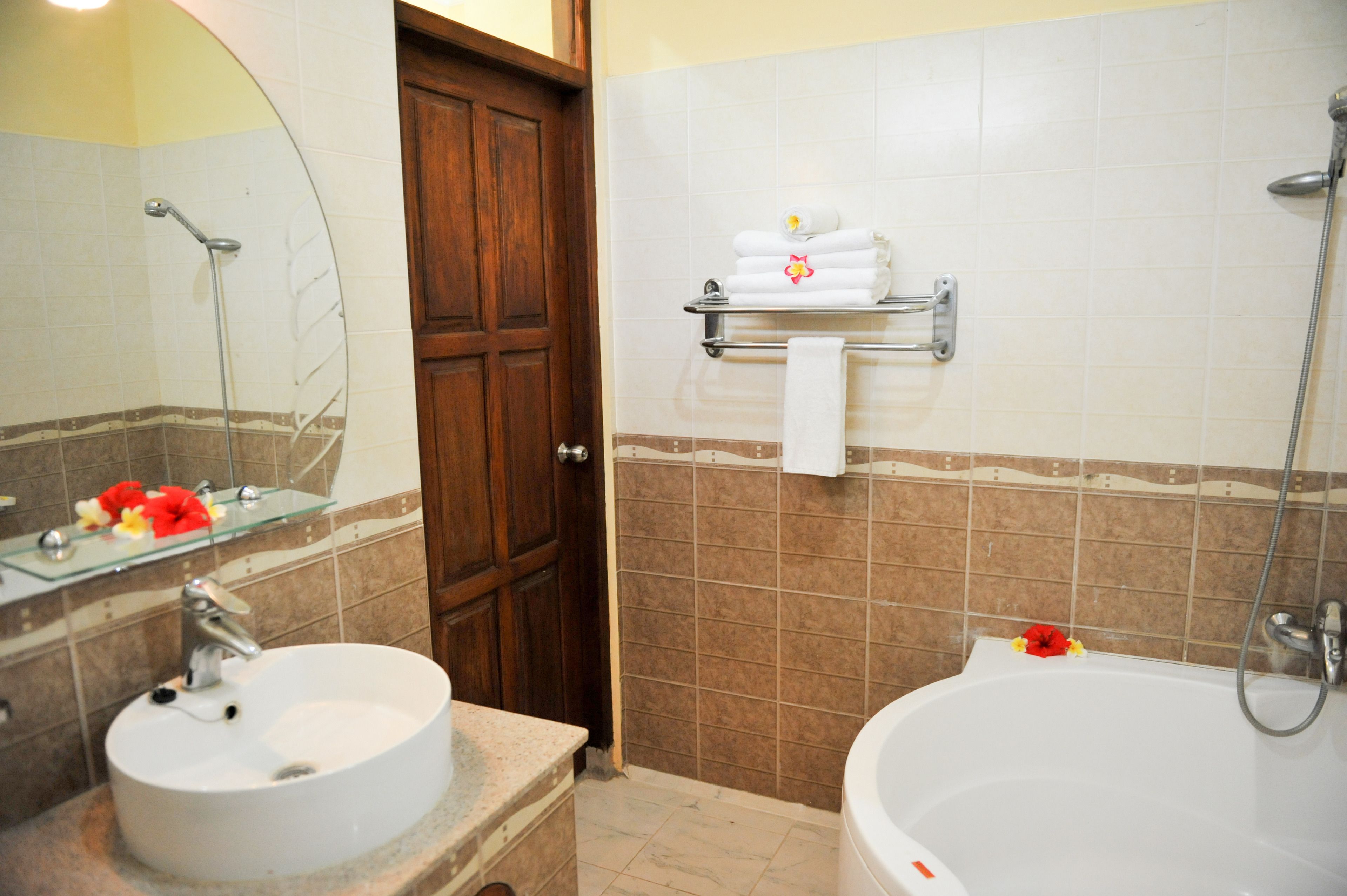 Un baño con dos lavamanos, una ducha, un estante de vidrio con toallas y una puerta de madera.