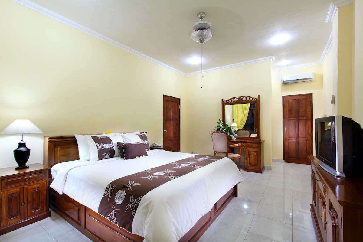 A hotel room with a large bed, wooden furniture, a television, and an air conditioning unit.