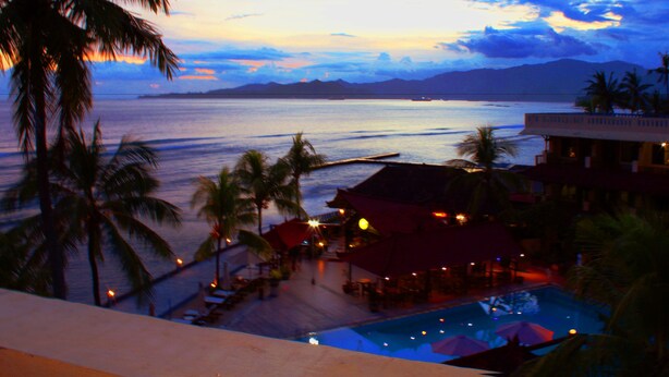 Ein Resort mit Pool, Palmen und Blick auf das Meer im Abendlicht.