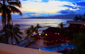 A resort with a pool, palm trees, and a view of the ocean at dusk. - Bali Palms Resort (Manggis)