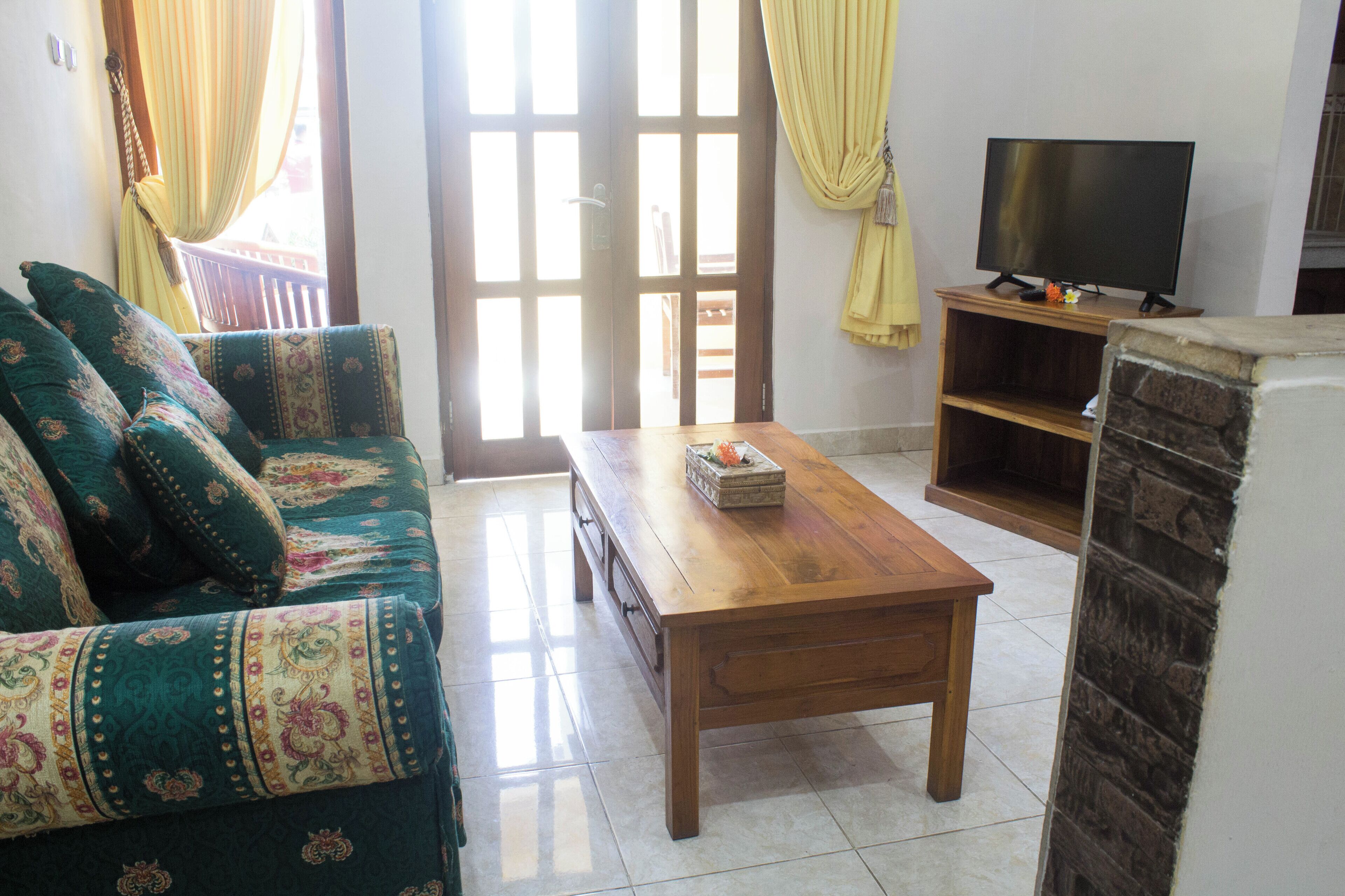 A living room with a sofa, a wooden coffee table, a TV on a stand, and a door with curtains.