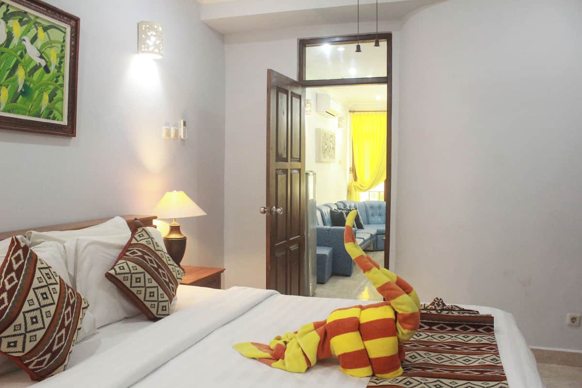 A hotel room with a bed, pillows, a lamp, and a stuffed toy.
