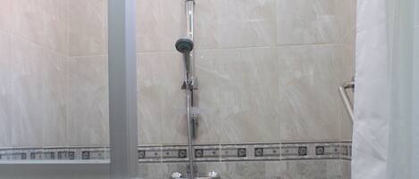 A bathroom with a shower, tiled walls, and a glass partition.