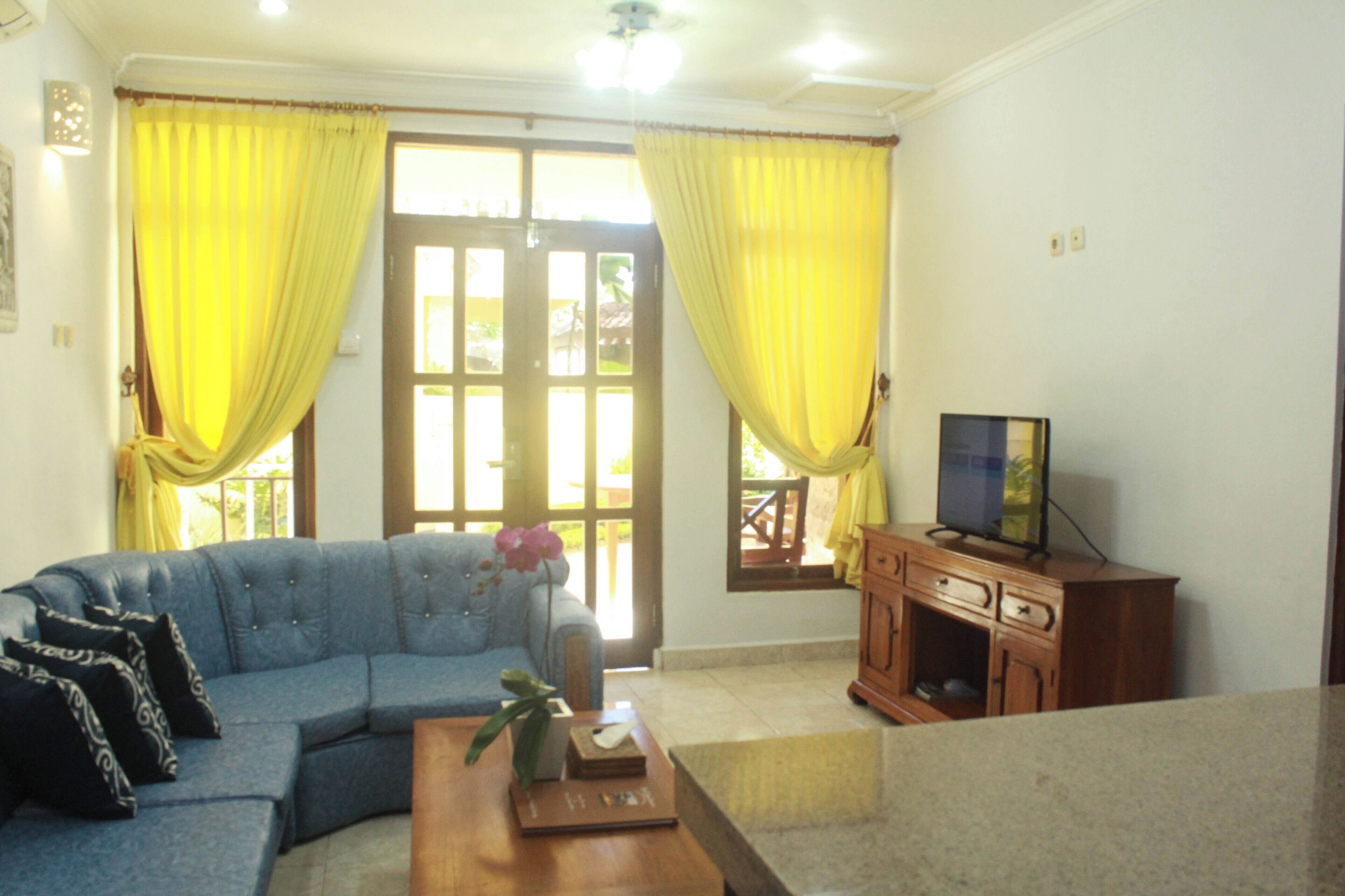 A living room with a blue sofa, yellow curtains, a wooden cabinet, and a television.