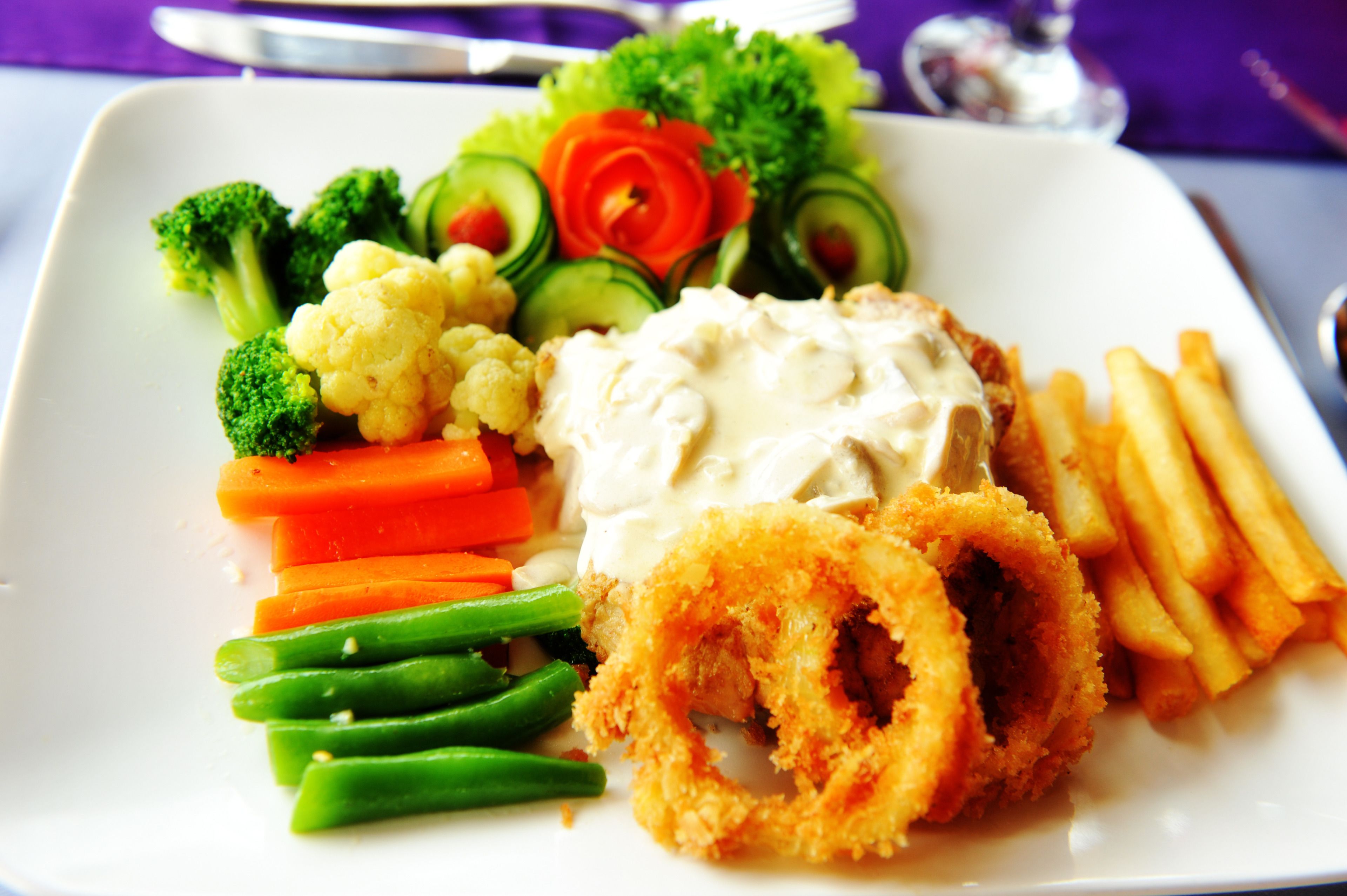 A plate of food with various vegetables and a breaded item, possibly chicken, alongside French fries.