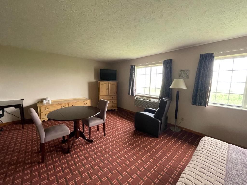Een hotelkamer met een bed, een bureau, een stoel, een tafel, een televisie, een lamp en een raam met gordijnen.