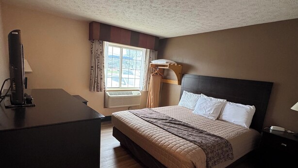 A hotel room with a bed, bedside table, and a desk with a computer. - The Woodridge Inn (Connersville)