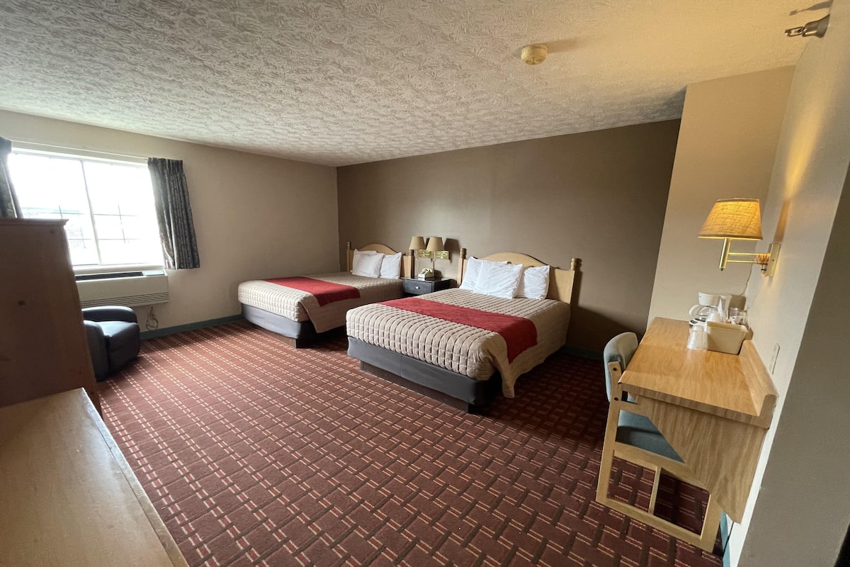 A hotel room with two beds, a desk, a chair, a window with curtains, and a ceiling with a textured pattern.