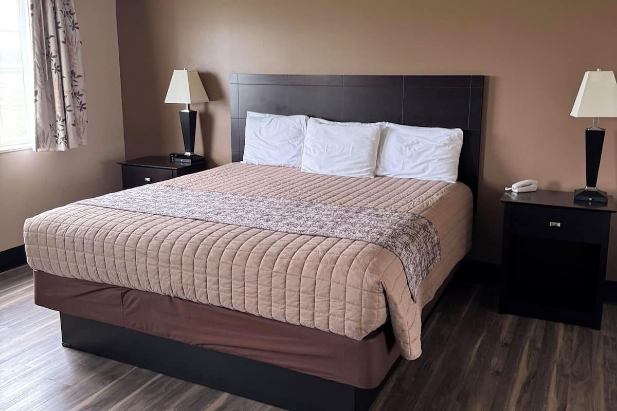 A neatly made bed with a brown quilt, two bedside tables with lamps, and a window with curtains.