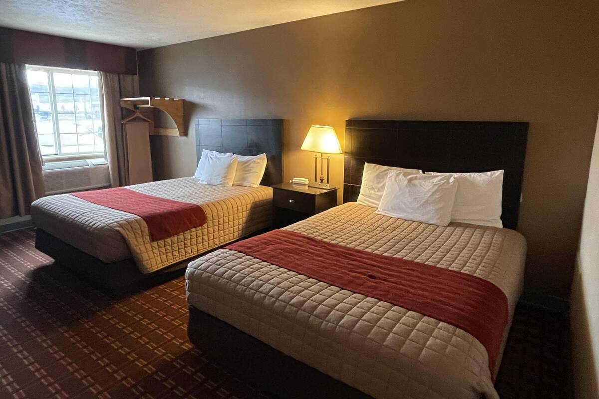 Two double beds with headboards, a bedside table with a lamp, and a window with curtains.
