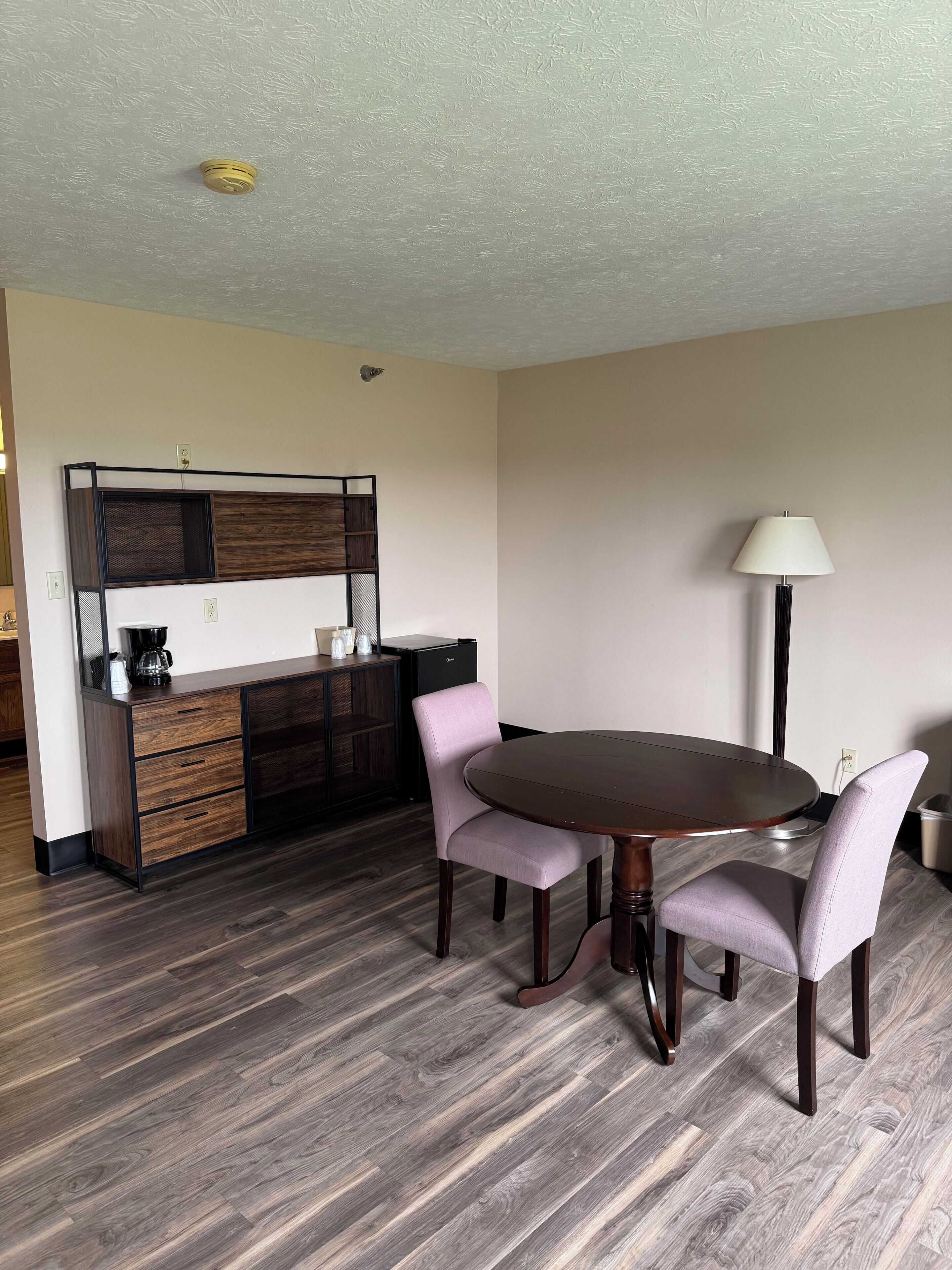 A dining area with a round table and four chairs, a coffee maker, and a lamp.