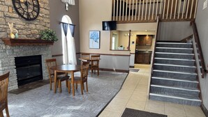 A spacious living area with a fireplace, a dining table with chairs, a staircase, and a kitchen in the background. - The Woodridge Inn (Connersville)