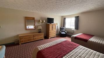 Habitación de hotel con dos camas, un aparador de madera, un televisor, una silla y una ventana con cortinas.